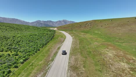 car travels on gravel road revealing blue lake tekapo in mackenzie basin, aerial