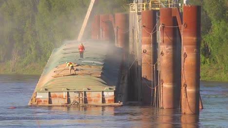 los trabajadores cargan una barcaza de grano a lo largo del río mississippi cerca de un gran molino