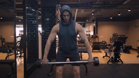 hombre haciendo un ejercicio de fila vertical de agarre ancho en posición doblada para el entrenamiento de los músculos del delto trasero y medio en un gimnasio cubierto - vista frontal