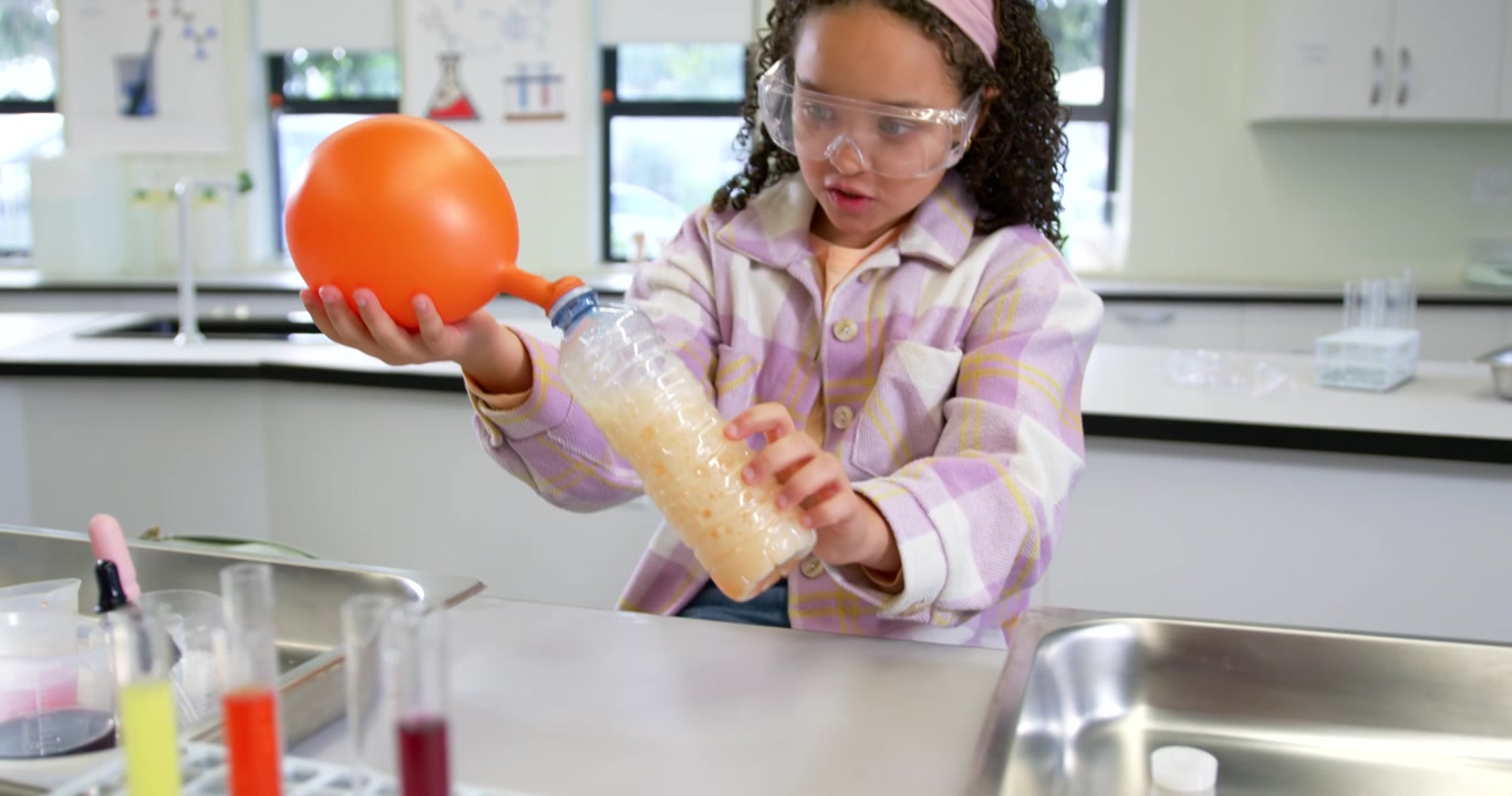 Niño afroamericano realizando una reacción que crea gas, inflando un globo en una botella en un laboratorio escolar.