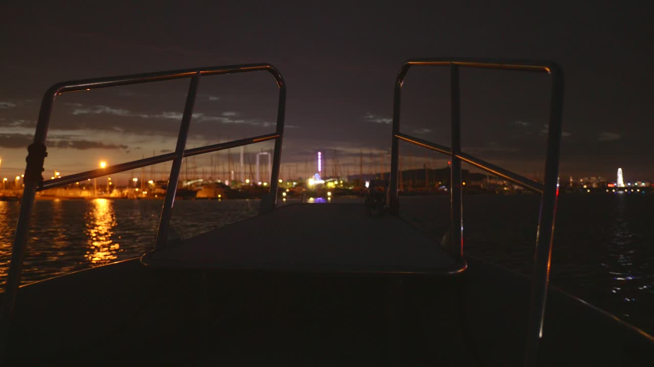 Front POV view from a boat at night in Agde, France, with city harbor lights glowing across the calm waters