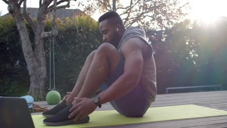 Hombre-Afroamericano-Enfocado-En-Entrenamiento-Físico-Haciendo-Abdominales-En-Cubierta-En-Un-Jardín-Soleado,-Cámara-Lenta