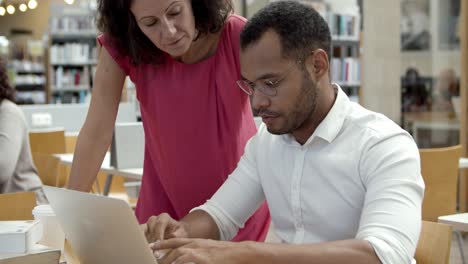 Side-view-of-serious-colleagues-working-with-laptop-at-library