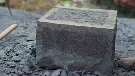 handheld shot showing a craftsman shaping the edge of a brick made from cancagua stone in the city of ancud on the island of chiloe