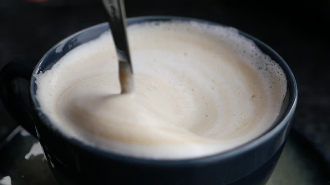 Close up of a cup of cappuccino with a spoon stirring the foam