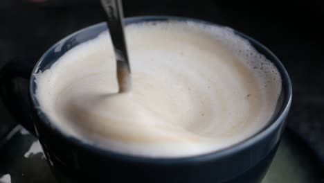 close up of a cup of cappuccino with a spoon stirring the foam