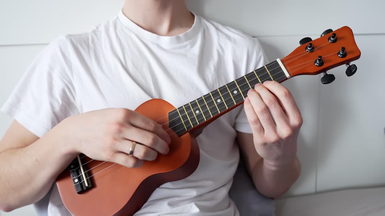 A close-up shot of a man playing a ukulele at home, with only his upper body visible, creating a cozy and intimate music moment.