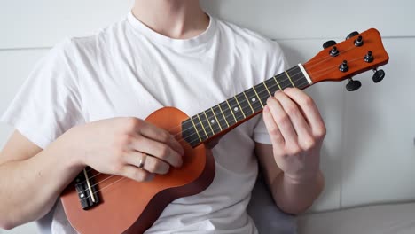 a close-up shot of a man playing a ukulele at home, with only his upper body visible, creating a cozy and intimate music moment.