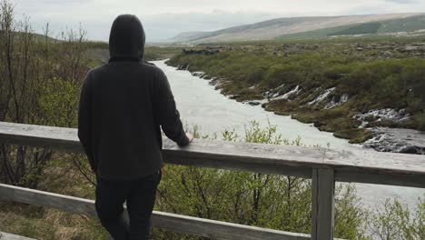 handsome young male with a hoodie looking at a beautiful view at barnafoss waterfall in iceland all alone and waiting for someone