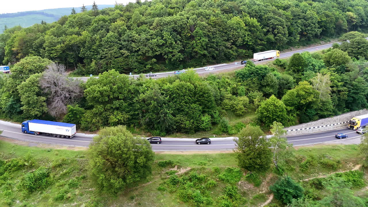 Traffic moves through hilly trees. Vehicles navigate winding roads surrounded by lush greenery in a scenic hilly area during daytime