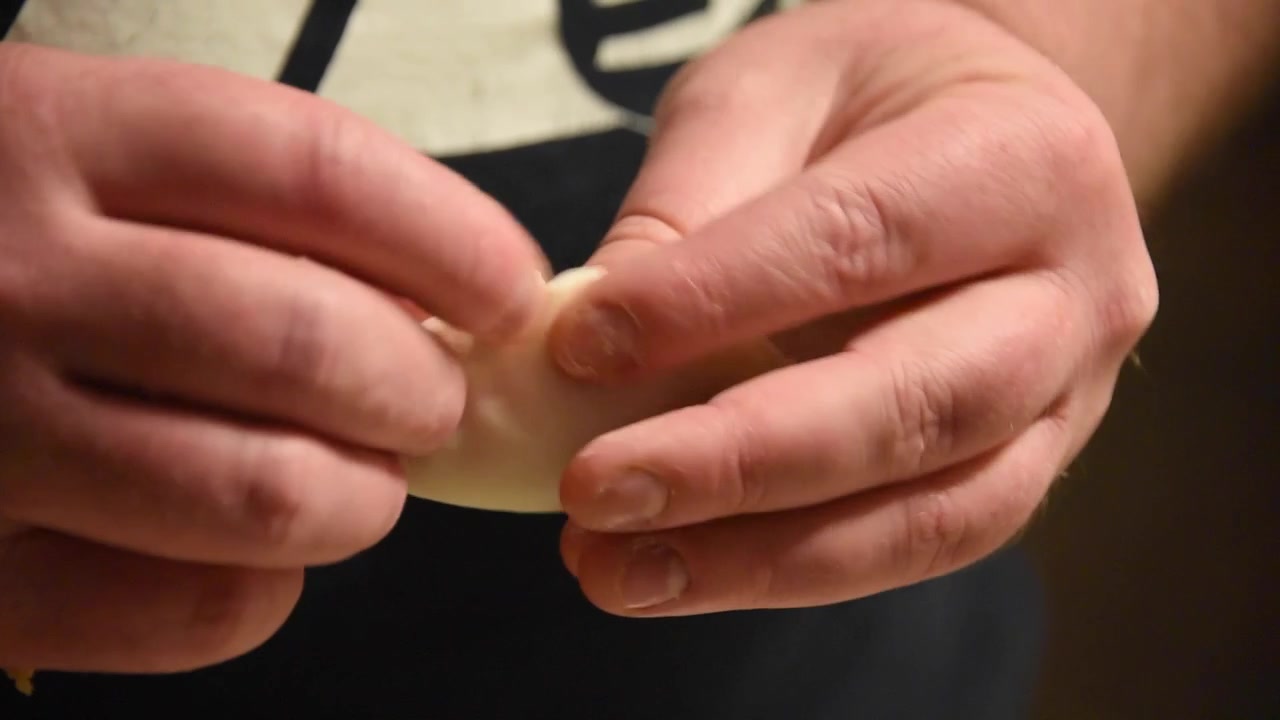 Pemandangan close-up tangan pria yang dengan terampil menyiapkan gyoza tradisional Jepang. Koki dengan hati-hati melipat dan mengerutkan kulit adonan.