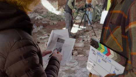 vue rapprochée de deux collègues de production méconnaissables parlant et lisant un document sur le film dans un bâtiment en ruine tandis que d'autres collègues se préparent pour l'enregistrement