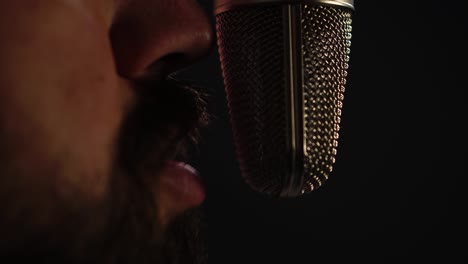 boca de un hombre con barba hablando cerca de un micrófono de estudio profesional, de cerca