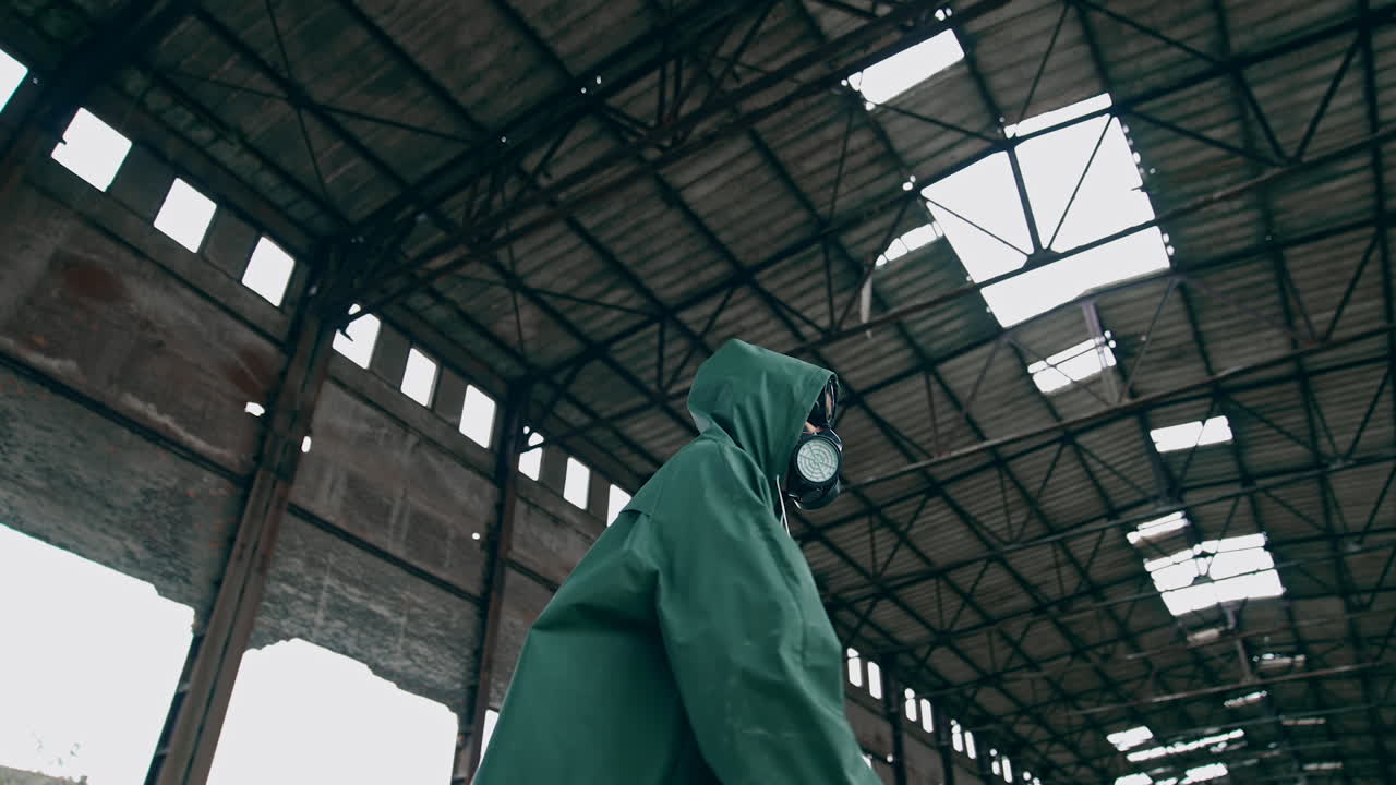 Human in a respirator and a hood is standing in abandoned building. Survivor on the background of a ruined building with holes on roof.