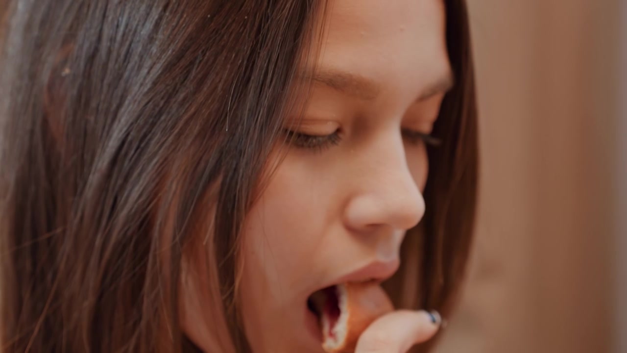 Adolescente caucásica mirando de reojo en una sala de estar tranquila, masticación sutil, pensamientos lejanos, grano de película suave, paleta cálida, primer plano medio espontáneo, estado de ánimo introspectivo, duda juvenil.