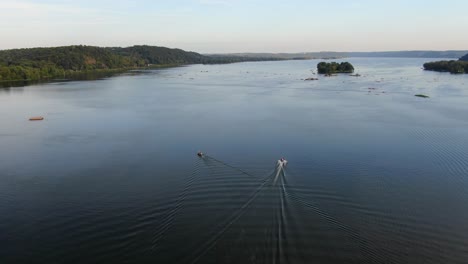 Peaceful-rising-aerial-drone-shot-of-boats-and-their-wake-on-blue-Susquehanna-River-at-sunset