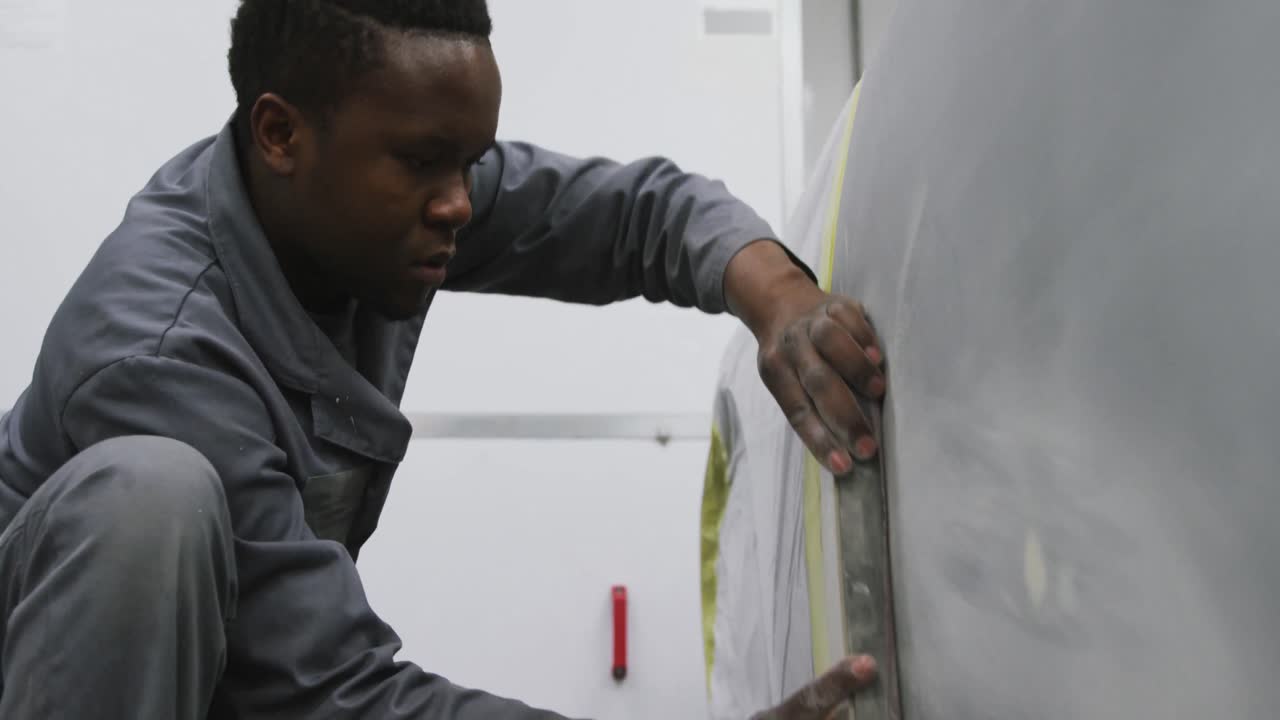 African American male car mechanic working in a township workshop and polishing a side of a car