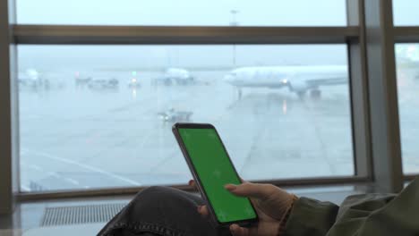 chica se sienta y usa un teléfono inteligente con una pantalla verde en el aeropuerto