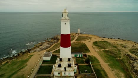 iconic lighthouse building on ocean coastline, aerial fly away shot