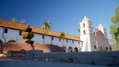 the historic santa barbara mission with a fountain and the red tile roof and spanish catholic architecture in california with palm trees