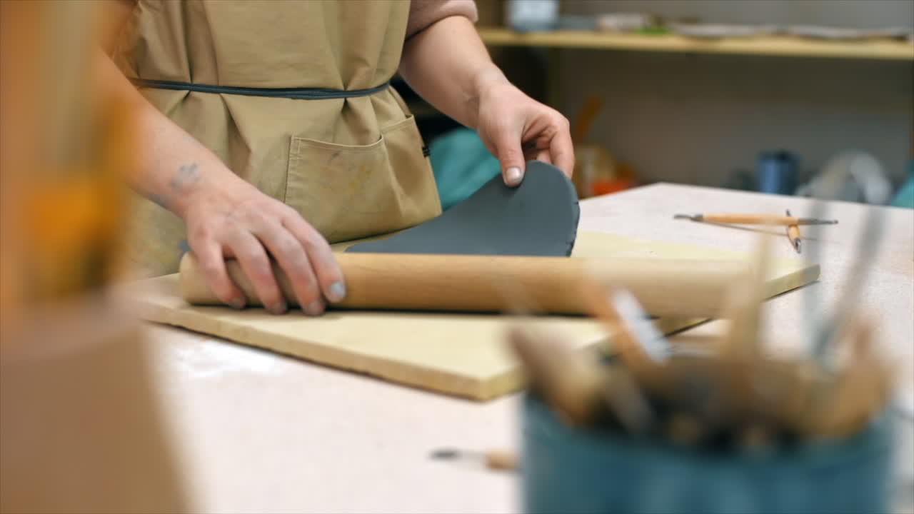 The master of sculpting pottery working in a studio. Rolling out the clay with a rolling pin. Tools on the table. Slow motion