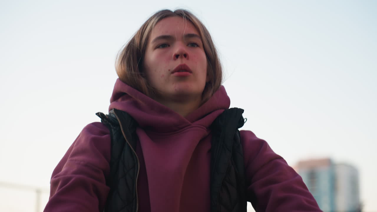 Athlete in hoodie and vest squatting with intense gaze on urban court at sunset, tall buildings blurred in background conveying strength, focus and determination during outdoor training session
