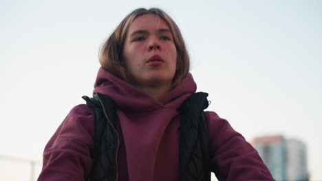 athlete in hoodie and vest squatting with intense gaze on urban court at sunset, tall buildings blurred in background conveying strength, focus and determination during outdoor training session
