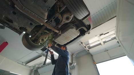 young car mechanic at repair service station inspecting car wheel and suspension detail of lifted automobile. bottom view.