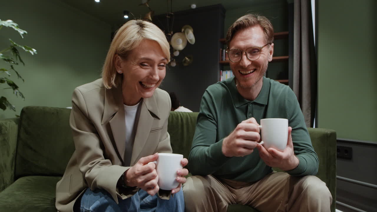 A man and a woman relaxing and drinking beverages on a green couch