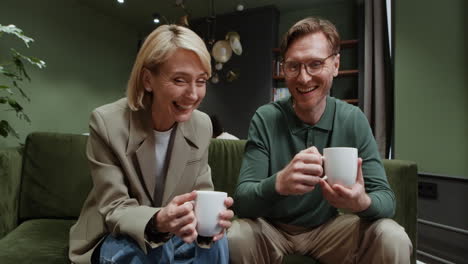a man and a woman relaxing and drinking beverages on a green couch