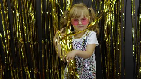 Happy-child-dancing,-playing,-fooling-around-in-shiny-foil-fringe-golden-curtain.-Little-blonde-girl