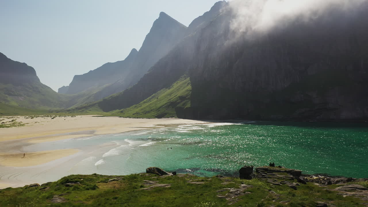 Cinematic wide aerial shot of three people swimming at Horseid Beach in turquoise blue water