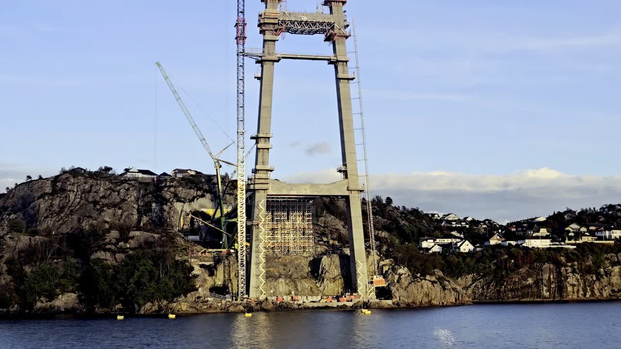 Detailed handheld shot showing Sotra Link bridge tower with scaffolding and cranes by the fjord