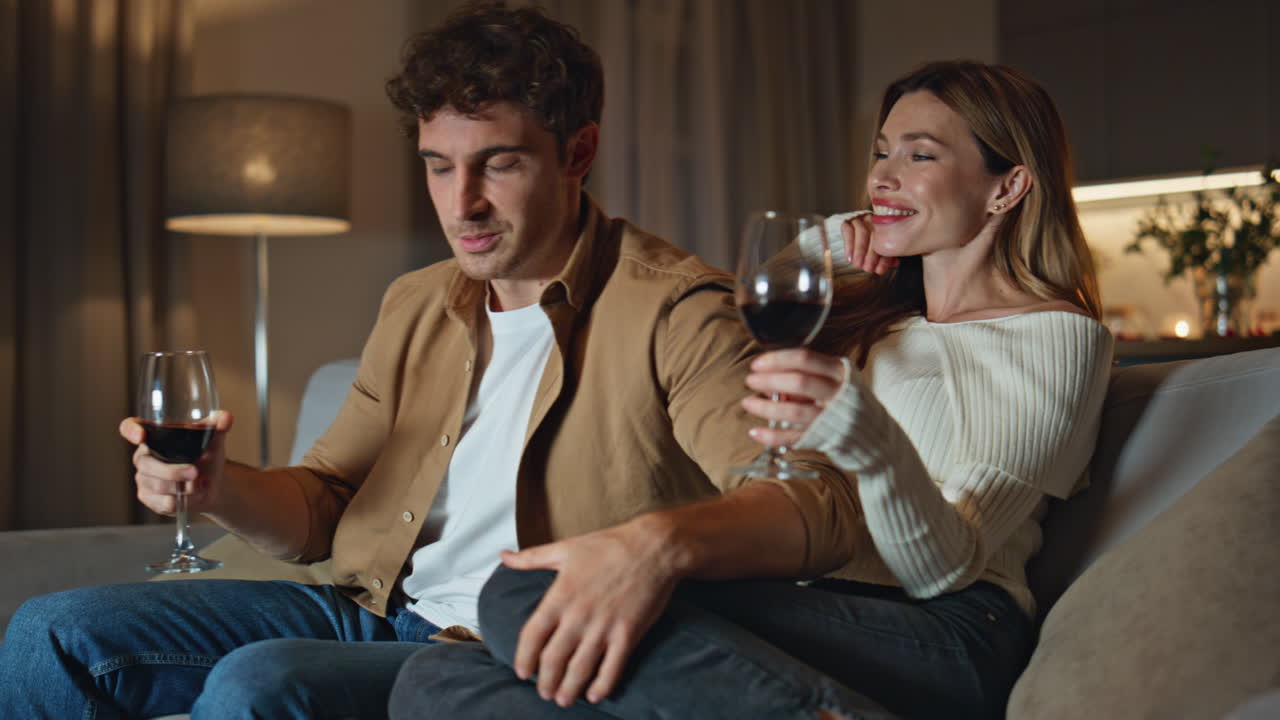 Caring boyfriend giving wine glass to girlfriend sitting at room couch close up.