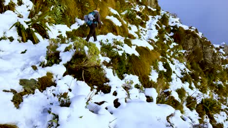 vista posterior de una mujer solitaria trekker, recorriendo el terreno montañoso empinado y nevado de la pista routeburn