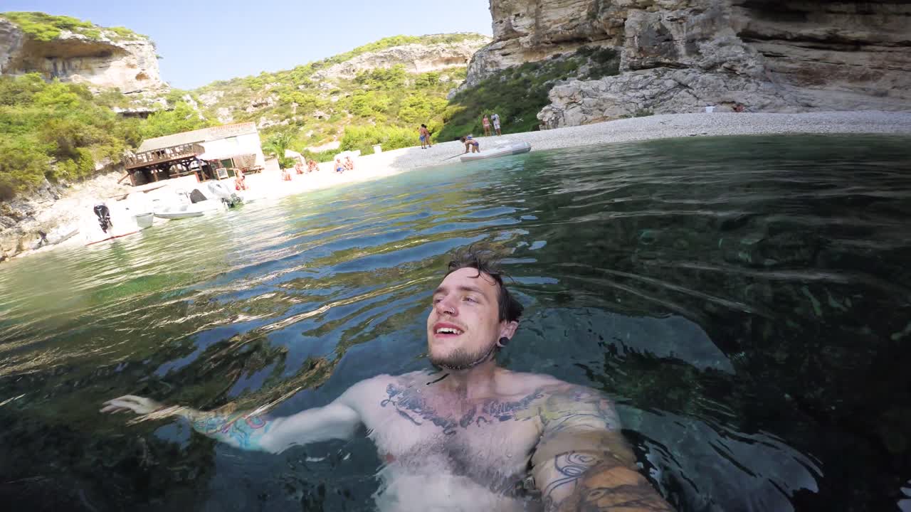 joven nadando de espaldas en una cala oceánica mirando hacia el cielo y los acantilados que rodean el agua clara