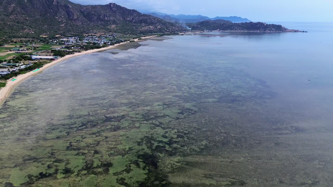 Very high drone flies forward with an upward pan, revealing the beach on the left and ahead, distant mountains, and a clear horizon in Vietnam.