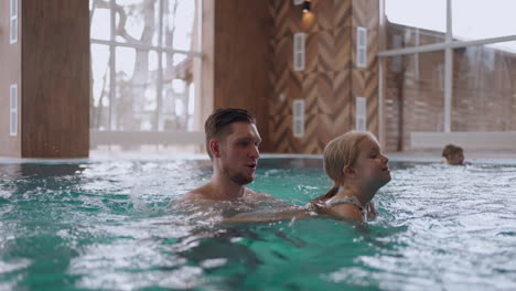 modern balneology center with thermal pool indoor adult man is teaching his little daughter to swim