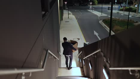 Business-Man-Walking-Down-Stairs-At-Night-Holding-A-Box-of-Files-Documents