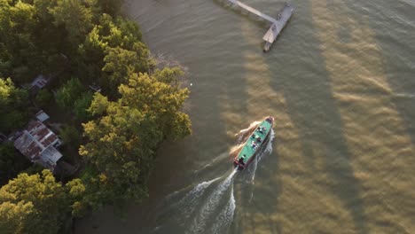 Toma-Aérea-De-Un-Barco-De-Autobús-Flotando-En-El-Río-Paraná-Durante-La-Puesta-De-Sol-Dorada---Argentina,-Sudamérica---Toma-En-órbita