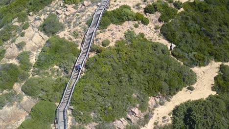 toma aérea siguiendo a una pareja subiendo por una pasarela de madera en un cabo en una playa del sur de españa