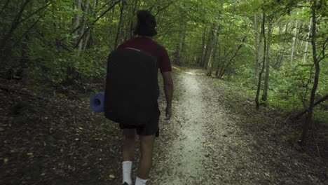 a young latino is walking a forest path with a yoga mat in his hand