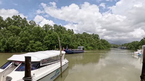 a speedboat approaches a wooden pier along a calm mangrove river under bright daylight, with lush greenery and partly cloudy skies in ko phayam
