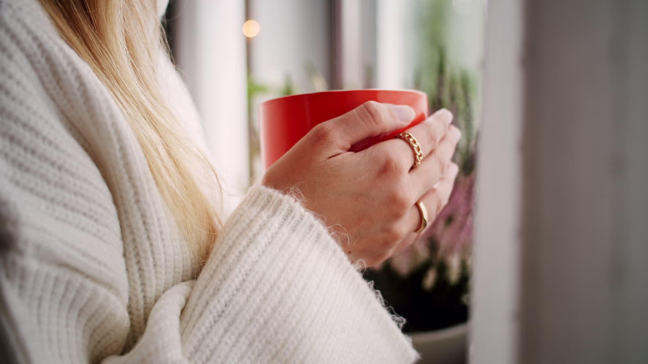 창가에 서 있는 오렌지 머그잔을 들고 있는 젊은 여성, 클로즈업