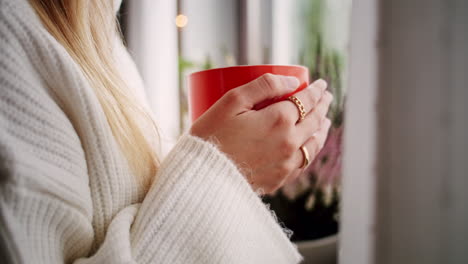 Junge-Frau-Hält-Einen-Orangefarbenen-Becher-Am-Fenster,-Nahaufnahme