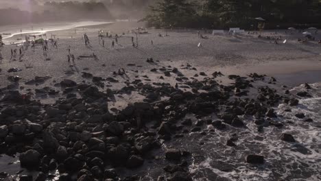 drone moves backwars into the acean revealing a beach at the golden hour with a lot of action going on in the shore