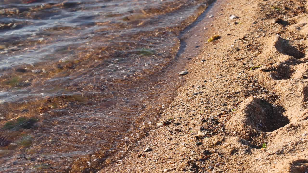 파도가 모래 바가 브라이튼 해변에서 발자국을 지워버립니다.