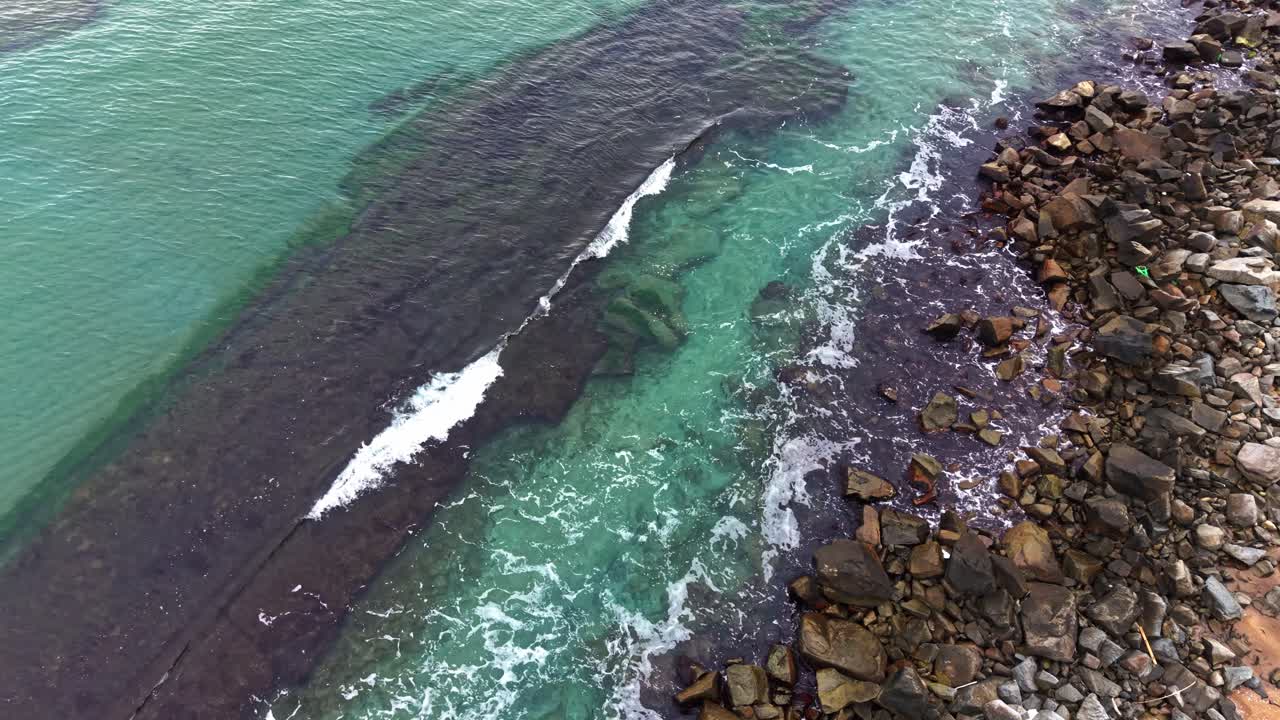Vibrant turquoise waters meet rocky shoreline from an aerial view
