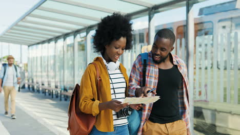 african american young couple of tourists walking with map and looking for right route in bus station