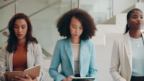 three businesswomen walk down a staircase in an office building.